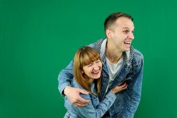 Young cheerful couple smiling, hugging, wearing, Looking away, denim clothes on a green background