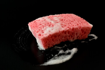 Red sponge with soap foam on a black background.