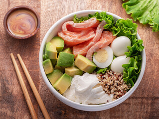 Salmon quinoa bowl with greens and vegetable on the wooden table. Balance in bowl. Top view.