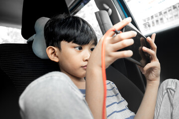 An Asian boy enjoying playing online game on smartphone inside a car