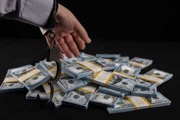 On a black background, a handcuffed hand reaches for a pile of dollar bills. A hand wants to steal...