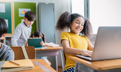 Portrait of black girl using computer to learn lessons in elementary school. Student boy studying in primary. Children with gadgets in classroom. Education knowledge, technology internet network.