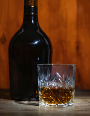 A glass and a bottle of strong alcohol on a background of oak barrels in a bar on the table. Close-up. Vertical
