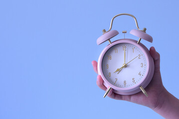 A person is holding a pink alarm clock that is set to the time of 8:00