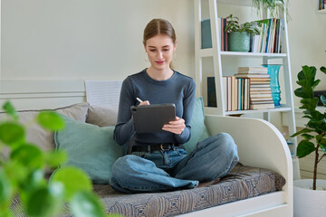 Young female teenager with digital tablet, stylus drawing illustrating sitting at home