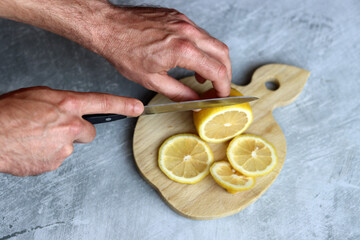 Close-up of man's hands cutting lemons on wooden cutting board. Lemonade preparation in process. 