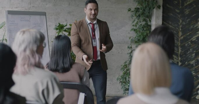 Joyful coach playing ball game with audience teaching confidence and self development in business hall. Personal growth and seminar concept.