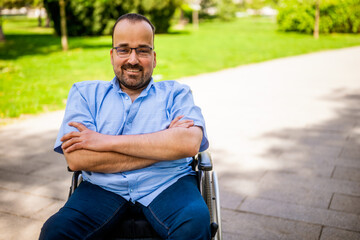 Portrait of happy man in wheelchair. He is enjoying sunny day in city park.