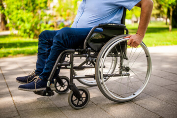 Close up image of man in wheelchair rolling on pathway in park.