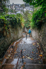 Stairs of an old alley. A woman in a blue raincoat walks down the stairs in the town of Morlaix,...