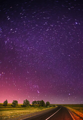Blue Night Starry Sky Above Country Asphalt Road In Countryside And Green Meadow. Night View Of Natural Glowing Stars.