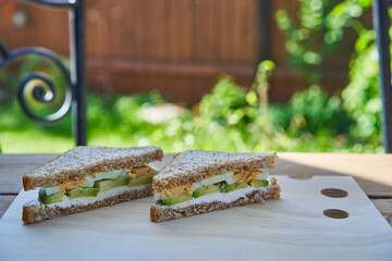 Sandwich made from wholegrain bread and spread by fresh cheese with slices of fresh riped avocado and hard boiled egg splited in two. Healthy and balanced snack or breakfast served in the garden.