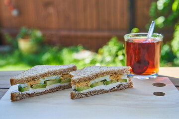 Simple, healthy and light breakfast with balanced nutritions served outside in the home garden during sunny summer morning. Meal constist from wholegrain sandwich with avocado and egg slices and tea.