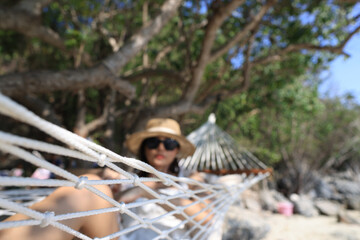 Portrait of a charming  young Asian woman with a  sunglass and happy smile leisure on a hammock swing around the beach sea and ocean with blue sky and white clouds for vacation