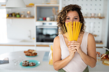 Portrait of smiling woman with spaghetti straps looking at camera while standing in the kitchen at...