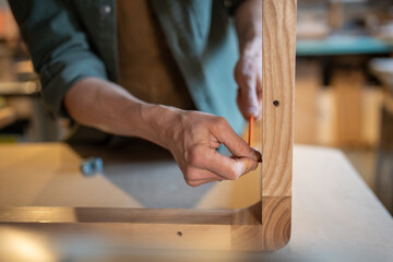 Male craftsman screwing furniture screws into the table, joins the pieces together, hands using hex...