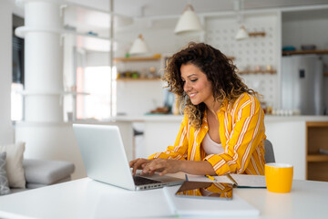 Beautiful smiling young woman working on laptop in her home office wearing stripped yellow shirt.