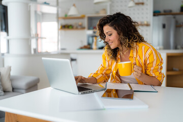 Smiling successful woman entrepreneur working on laptop while having coffee in home office.