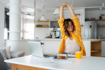 Carefree relaxed young adult woman stretching arms while using laptop at home and having a rest...