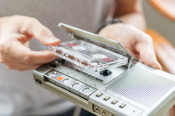 A male hand inserting a cassette tape into a retro cassette player. Vintage gadgets, nostalgic scene.