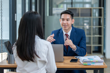 Two Asian professionals engaging in a thoughtful discussion at a business meeting, with a laptop and documents on the table.