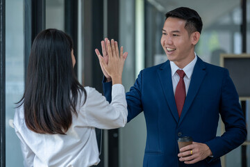 Asian male and female colleagues give each other a high five, celebrating success at their office...