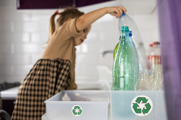 A girl carefully reaches across the kitchen table to place a plastic bottle in a trash box. Cute...