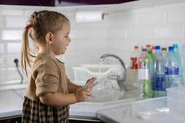 Cute child sorting plastic in the kitchen. The daughter follows the example of her parents and...