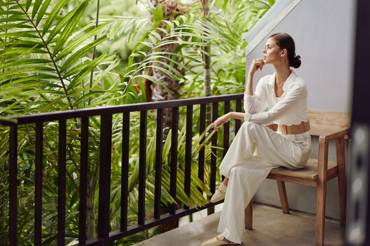 Happy Woman Enjoying Tropical Vacation on a Balcony Terrace, Smiling Under the Sunlight with Trendy Sunglasses A Young Girl Resting and Relaxing in a Stylish Apartment with a Beautiful View of the