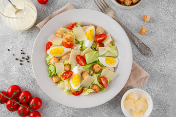 Caesar salad with lettuce, grilled chicken breast, boiled eggs, tomatoes, parmesan cheese and croutons in a ceramic plate on a concrete background. Top view.