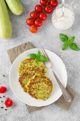 Zucchini fritters or zucchini pancakes on a white plate with fresh basil and sour cream. Top view, selective focus.
