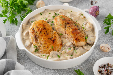 Roasted chicken breast with mushrooms in cream sauce on a white ceramic form on a gray concrete background. Comfort food. Top view.