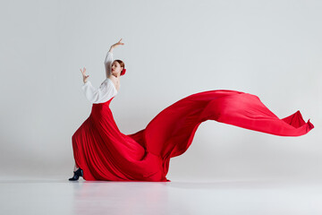 Passion. Female dancer in striking red costume performing flamenco dance against grey studio...