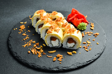 Japanese sushi with fish and cheese on a rustic dark background. Sushi rolls, nigiri, maki, pickled ginger, wasabi, soy sauce. Sushi set on a table.