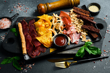 Antipasto, Appetizers for beer: nachos, basturma, prosciutto and grissini. On a dark background,...