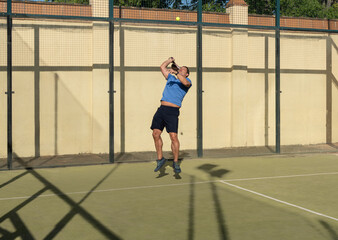 Athletic Man Performing High Jump Serve in Padel Tennis