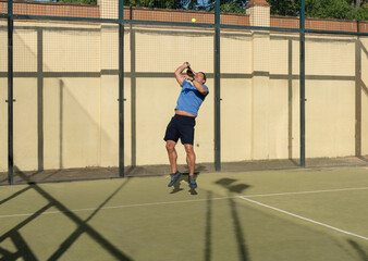 Obraz premium Athletic Man Performing High Jump Serve in Padel Tennis