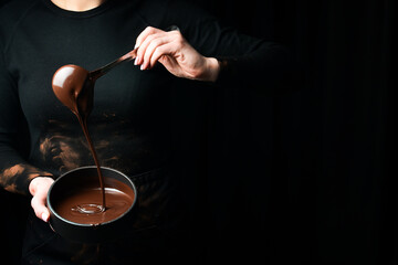 The chef scoops hot chocolate into a bowl. On a black background. Preparation of chocolate.
