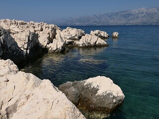 Pale rocky cliffs in a bay near Razanac, northern Dalmatia, Croatia. Velebit mountain visible in a haze on horizon. Summer daylight sunshine. 