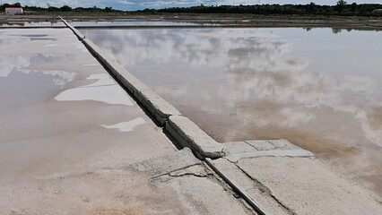 Low concrete barrier between two stages of sea salt production reservoirs, some dried salt visible...