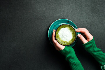 Green tea, hot matcha latte in white ceramic cup with saucer on young woman hand with cinnamon. Japanese hot milky beverage.