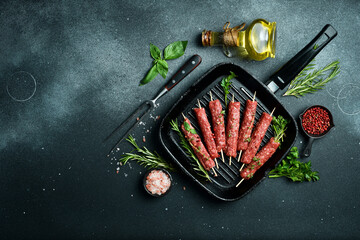 Lula kebab on skewers with spices and herbs in a pan. On a dark stone background. Top view.