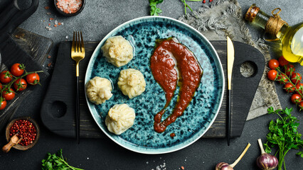 Khinkali, Georgian dumplings with meat filling served on a blue plate with adjika. Free space for...