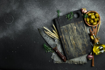 Kitchen cutting board, olives and oil. On a black stone background. Top view.