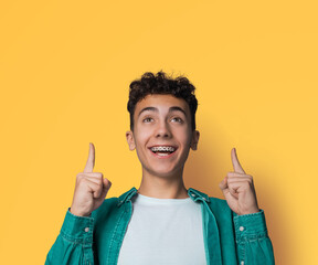 Excited black curly haired man in braces, open mouth, wear green denim shirt advertise pointing...