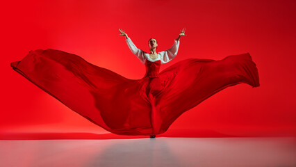 Passionate woman, flamenco dancer in stylish costume with skirt spreads like wings, performing against vivid red background. Concept of art of movement, classical dance, beauty, festival