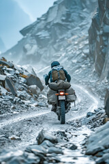 A man is riding a motorcycle on a rocky road. The road is covered in snow and rocks, making it a challenging and adventurous ride. The man is wearing a backpack