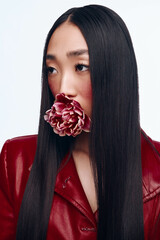 Beautiful woman with long black hair in a red jacket holding a flower in her mouth