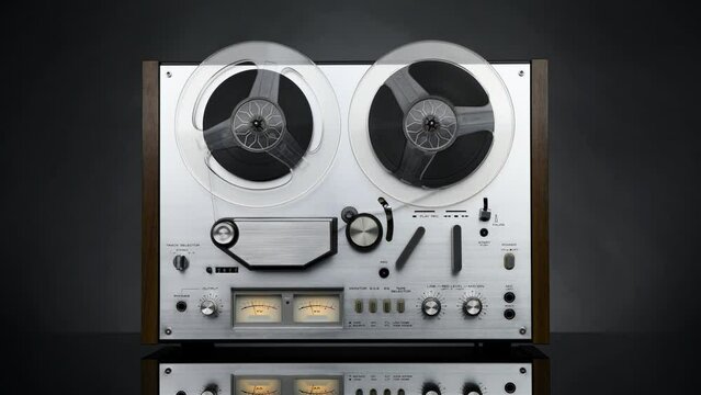 An old steel reel-to-reel tape recorder stands on a glass table and plays on a dark background in 4K. Front view