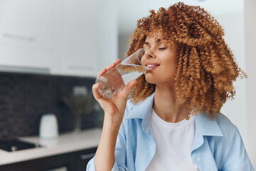 African American woman enjoying a refreshing drink of water in her home kitchen, looking beautiful...